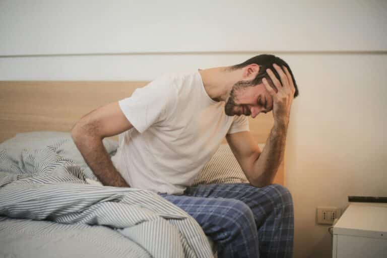 Photo d'un homme sur son lit qui a mal au dos et qui est fatigué, il va décidé de voir un chiropracteur à Annecy. Photo de Andrea Piacquadio: https://www.pexels.com/fr-fr/photo/jeune-homme-en-vetements-de-nuit-souffrant-de-maux-de-tete-le-matin-3771115/